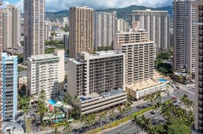 Un edificio de gran altura con varios balcones, una piscina en la azotea y palmeras a su alrededor.