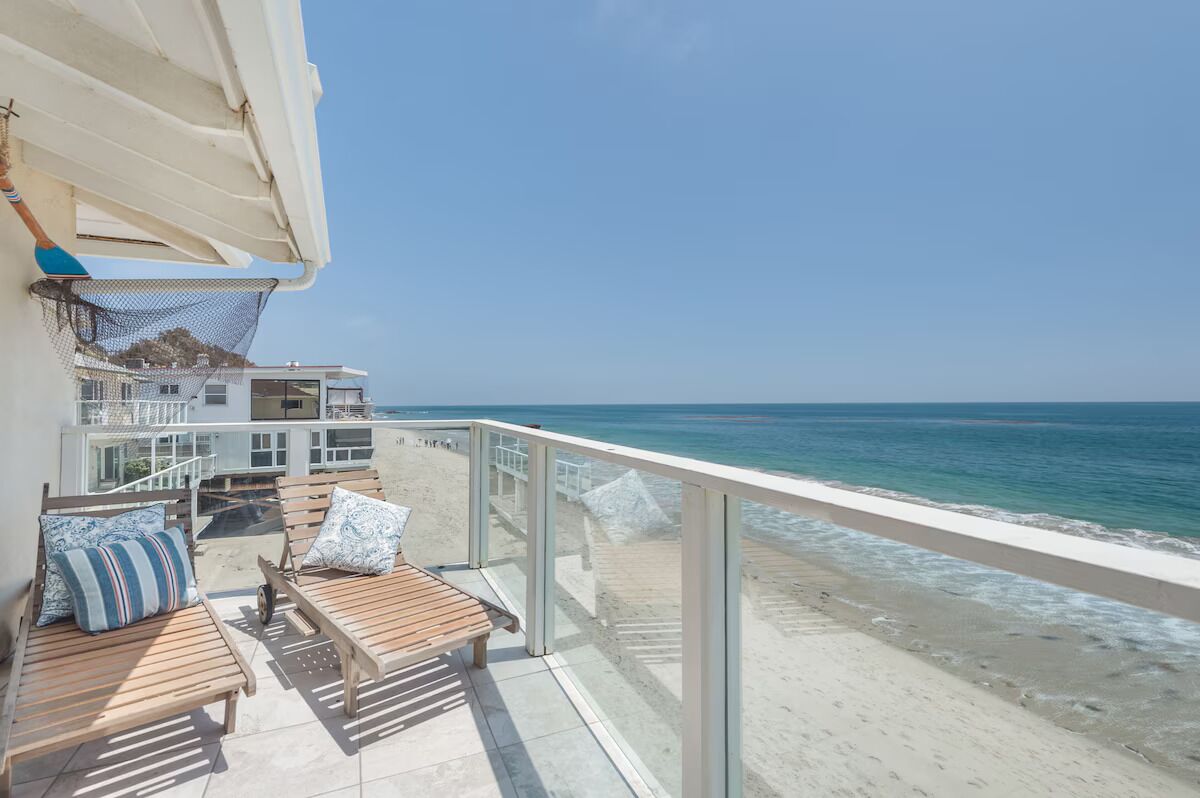 A balcony with wooden furniture, a white railing, and a view of the ocean.