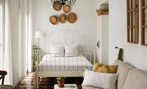 A bedroom with a white bed, a sofa, a checkered floor, and a wall with hats.