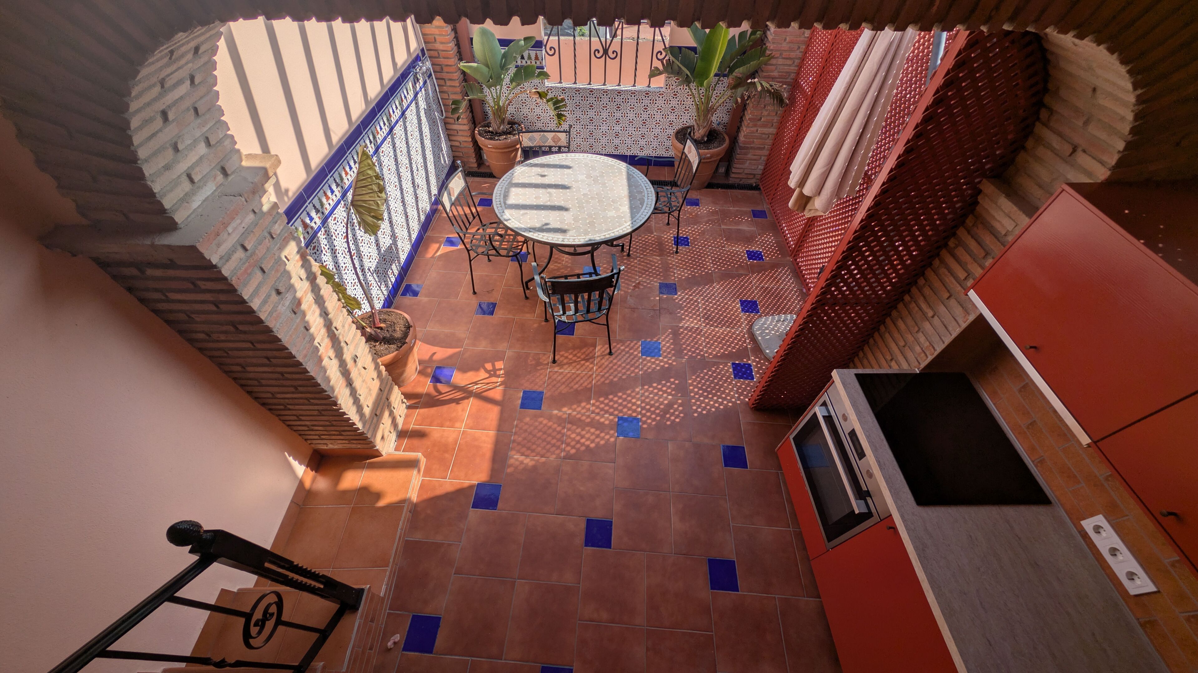 Un patio con una mesa redonda y sillas, plantas en macetas y un armario rojo.