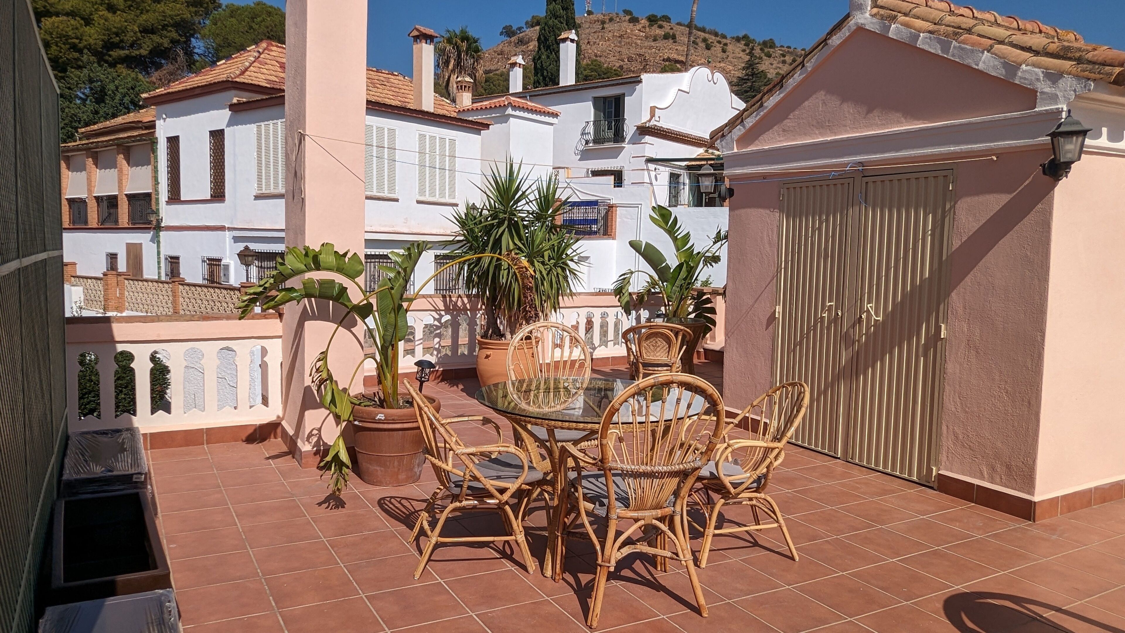 Una terraza con mesa y sillas, plantas en macetas y vistas a edificios cercanos.