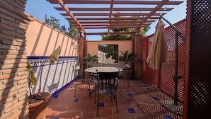 Eine Terrasse mit Tisch und Stühlen, einer Pergola, Topfpflanzen und einem Zierzaun.