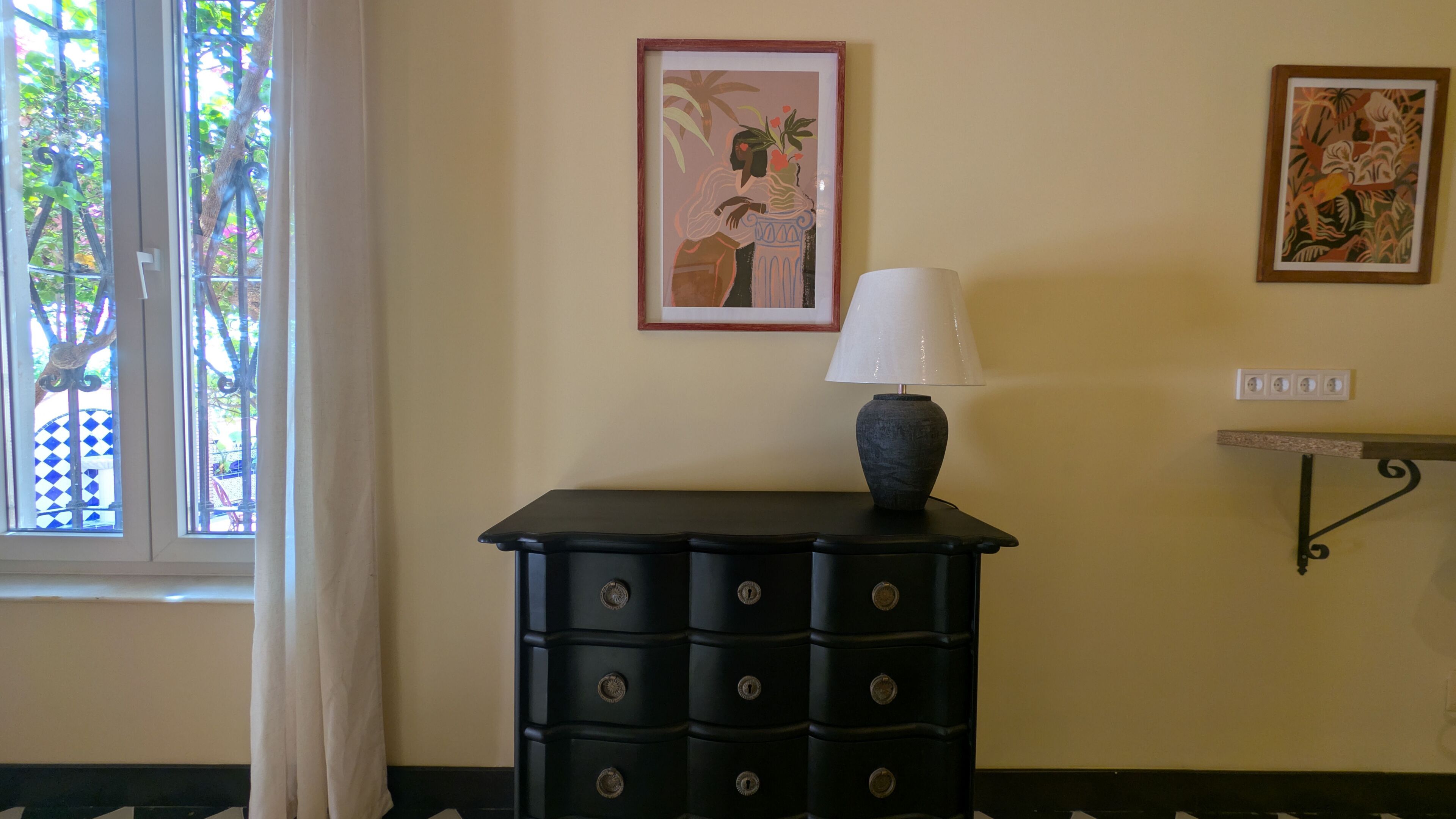 Una habitación con un aparador negro, una lámpara y dos cuadros en la pared.