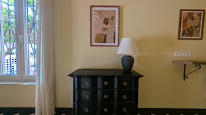 Een kamer met een zwarte dressoir, een lamp en twee ingelijste kunstwerken aan de muur.