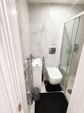 Un baño moderno con cabina de ducha de vidrio, inodoro blanco y lavamanos con cabezal de ducha manual.