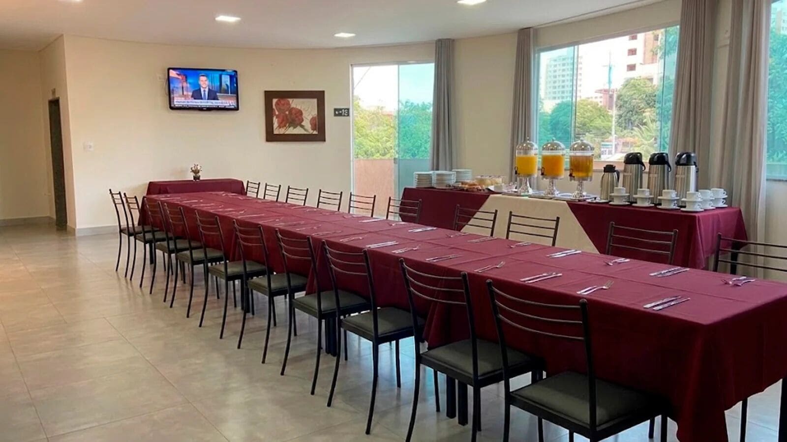 Sala de conferência com uma mesa comprida, cadeiras, uma televisão e um buffet com bebidas.