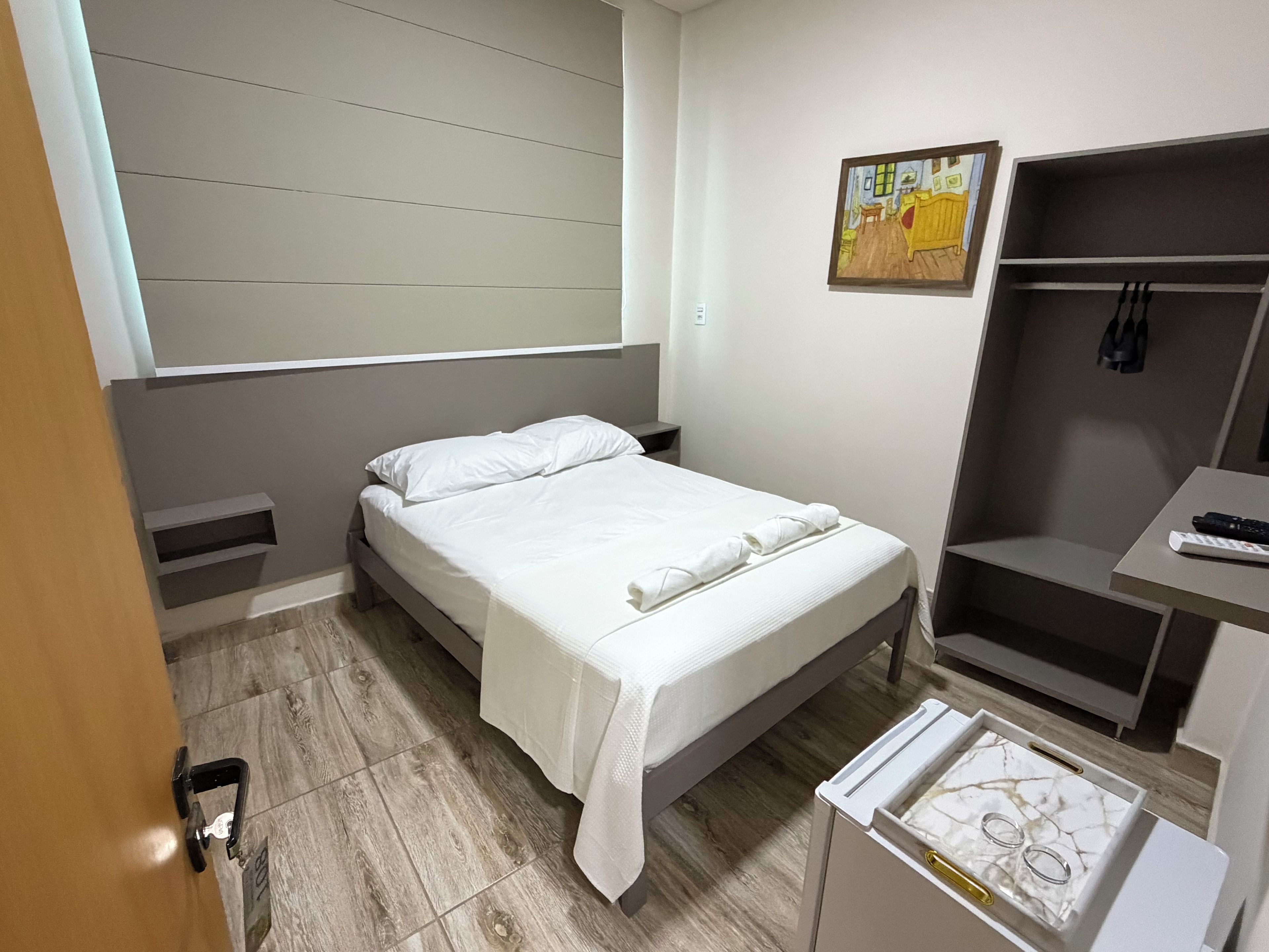 A bedroom with a bed, a bedside table, a wardrobe, a painting on the wall, and a window.