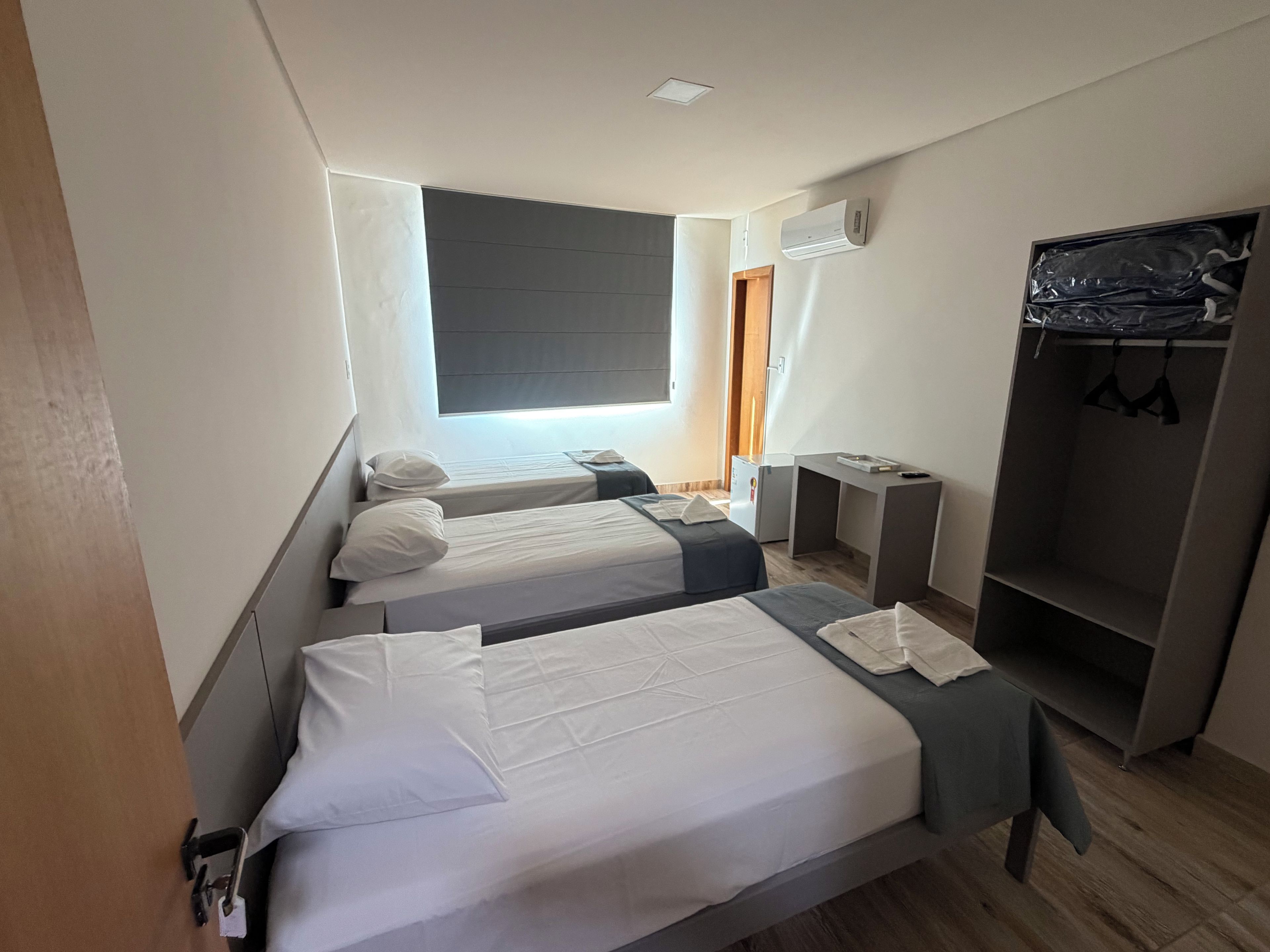 Habitación de hotel con dos camas, un armario, un escritorio y un equipo de aire acondicionado.