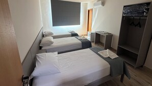 Habitación de hotel con dos camas, un armario, un escritorio y un equipo de aire acondicionado.