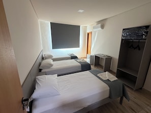 Habitación de hotel con dos camas, un armario, un escritorio y un equipo de aire acondicionado.
