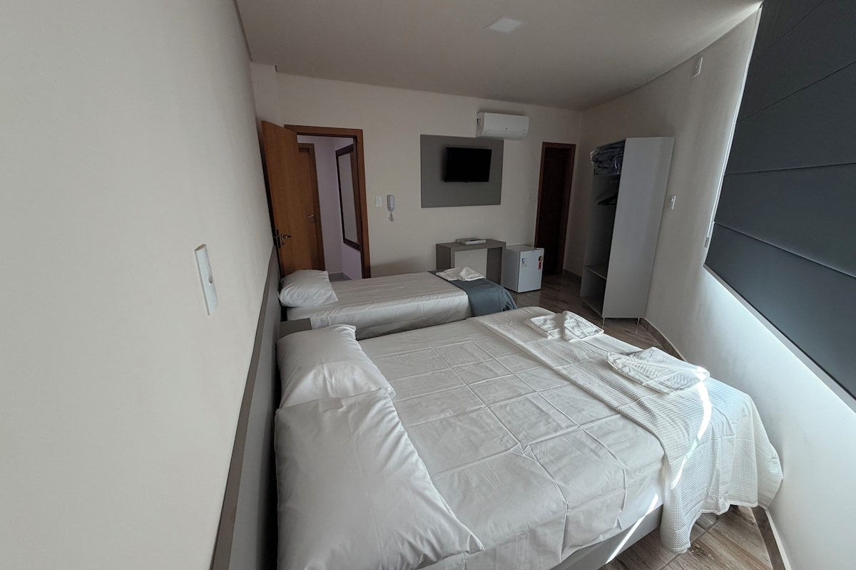 Habitación de hotel con dos camas, un escritorio, un armario y un televisor.