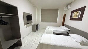 Habitación de hotel con dos camas individuales, un escritorio, una silla, un televisor y un armario.
