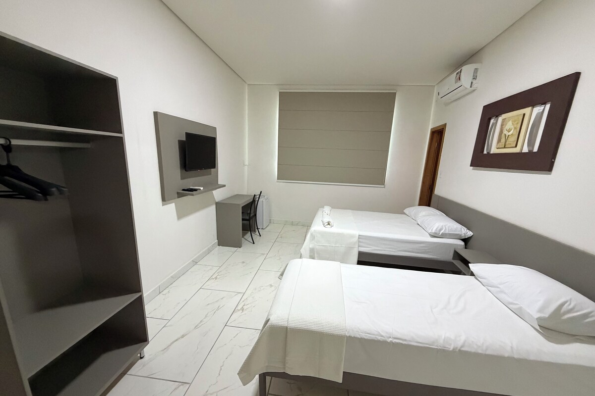 Habitación de hotel con dos camas individuales, un escritorio, una silla, un televisor y un armario.