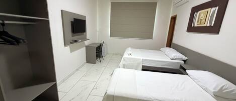 Habitación de hotel con dos camas individuales, un escritorio, una silla, un televisor y un armario.