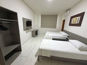 Habitación de hotel con dos camas individuales, un escritorio, una silla, un televisor y un armario.