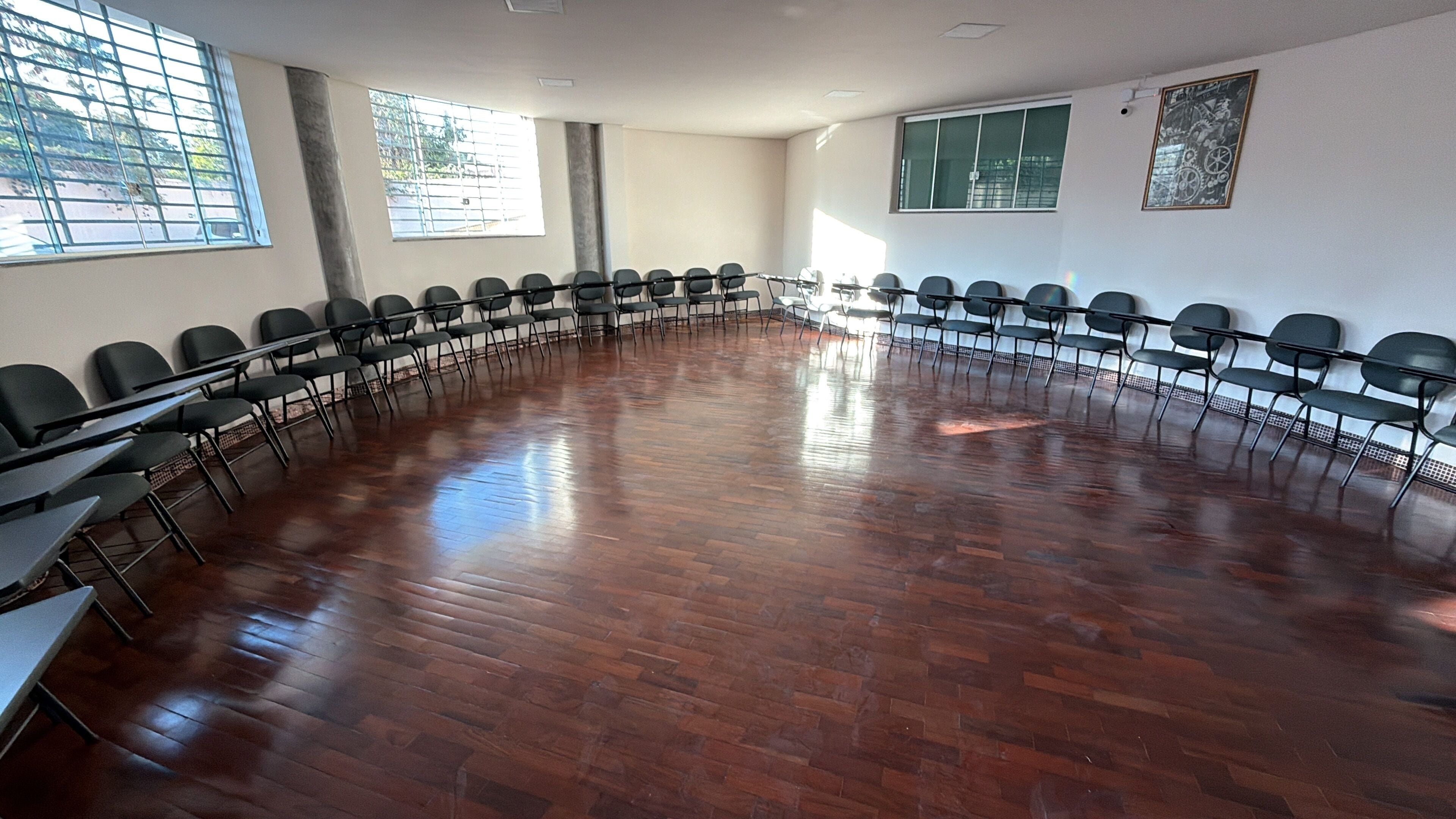 Sala de conferência com uma mesa comprida e cadeiras dispostas ao redor, amplas janelas e piso de madeira.