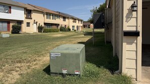 A residential area with a row of townhouses, a grassy lawn, and a utility box with a warning label. - Parkside Retreat - Central DFW - Near AT&T Stadium, DFW Airport & Arlington (Grand Prairie)