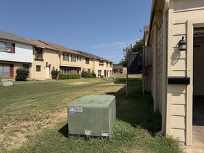 A residential area with a row of townhouses, a grassy lawn, and a utility box with a warning label. - Parkside Retreat - Central DFW - Near AT&T Stadium, DFW Airport & Arlington (Grand Prairie)