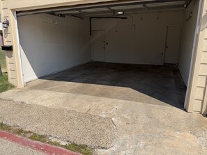 Een garage met een betonnen vloer, een gesloten garagepoort en een muur met een meterkast en een klein bordje.