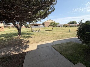 A residential area with a paved walkway, a tree, and houses in the background.