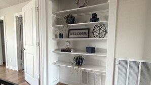 A hallway with a white built-in shelving unit containing decorative items and a welcome sign. - Parkside Retreat - Central DFW - Near AT&T Stadium, DFW Airport & Arlington (Grand Prairie)