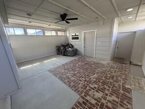 Een garage met een plafondventilator, een vloer met een baksteenmotief en een deur naar een overdekt gedeelte.