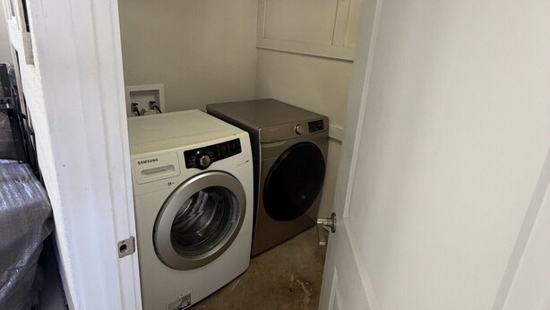 A laundry room with a front-loading washer and dryer, a shelf above the dryer, and a door leading to another room. - Parkside Retreat - Central DFW - Near AT&T Stadium, DFW Airport & Arlington (Grand Prairie)