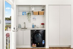 Ein kleiner Hauswirtschaftsraum mit Waschmaschine, Regalen mit Körben, einer hängenden Pflanze und einem Willkommensschild.