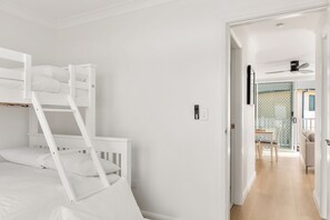Ein Zimmer mit Etagenbetten, einer Tür, die auf einen Balkon führt, und einem Deckenventilator.