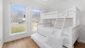 Een kamer met stapelbedden, grote ramen en een houten vloer.
