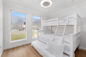 Ein Zimmer mit Etagenbetten, großen Fenstern und Holzboden.