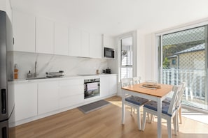 Een moderne keuken met witte kasten, een inbouwoven en een eethoek met een houten tafel en stoelen.