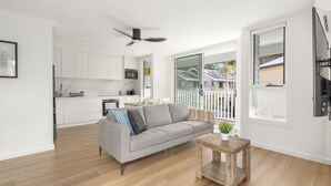 Een moderne woonkamer met een grijze bank, een houten salontafel en uitzicht op een balkon met een hekwerk.