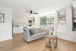 Ein modernes Wohnzimmer mit einem grauen Sofa, einem Holztisch und Blick auf einen Balkon mit Geländer.
