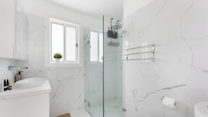 Een moderne badkamer met een douchecabine van glas, een wit wastafelmeubel en een toilet.