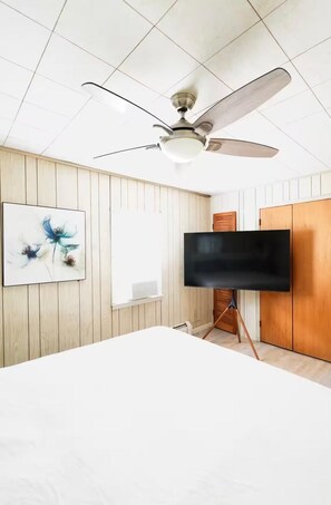A bedroom with a ceiling fan, a flat-screen TV on a stand, a bed, and a wall-mounted picture. - Perfect 6-bedroom house with AC in gorgeous Toms River (Toms River)