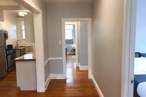 A narrow hallway with a kitchen on one side and a bedroom on the other.