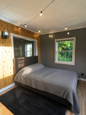 Ein Schlafzimmer mit Bett, einem Fenster mit Blick auf Grünflächen und einer Holzwand.