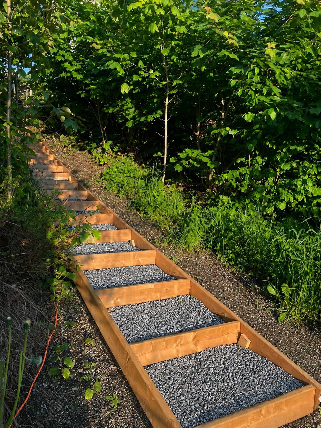 A wooden pathway with gravel steps surrounded by greenery.