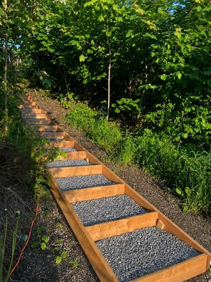A wooden pathway with gravel steps surrounded by greenery.