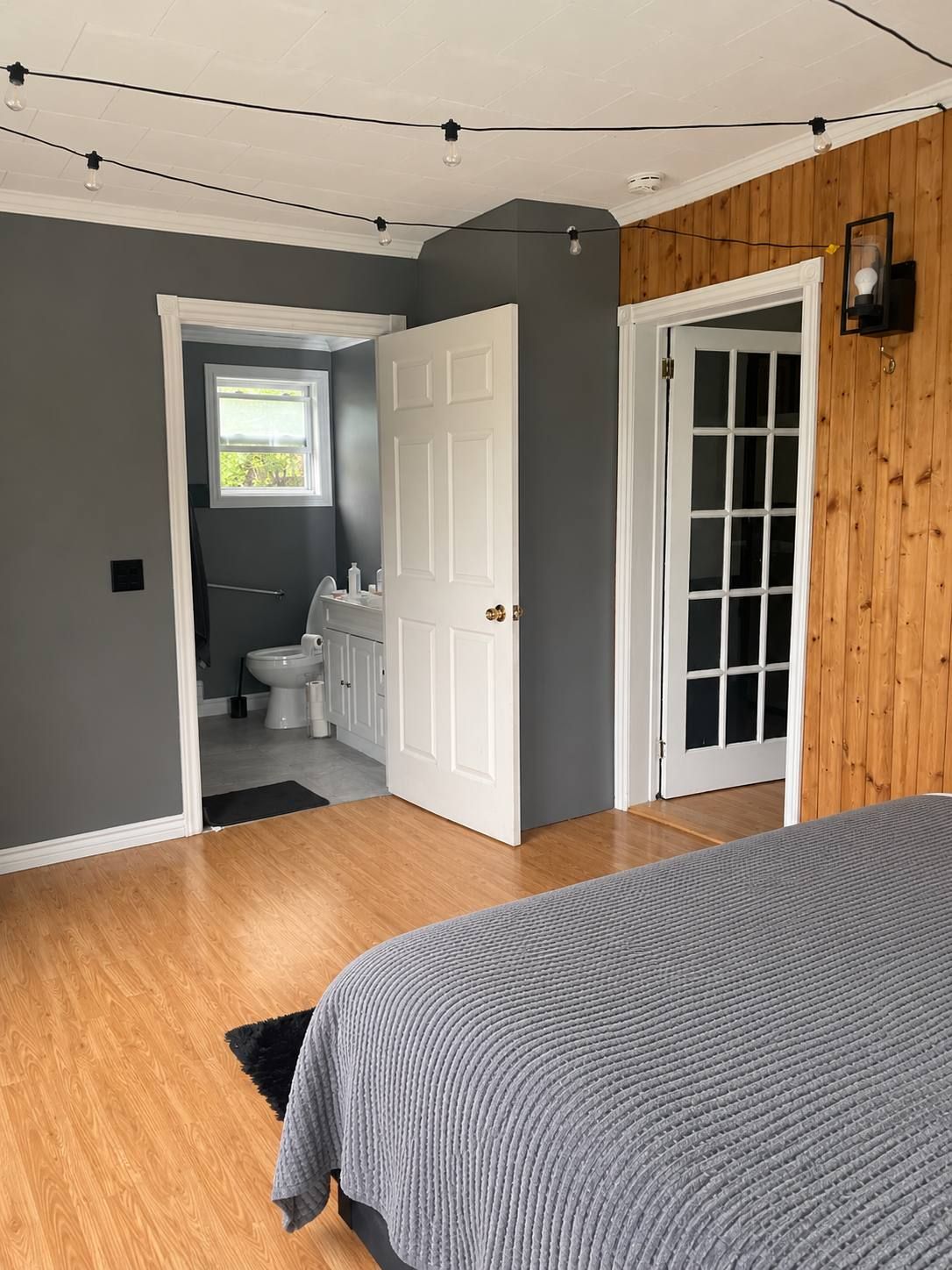 A bedroom with a bed, a door leading to a bathroom, and a view of the outside.