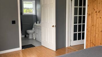 A bedroom with a bed, a door leading to a bathroom, and a view of the outside.