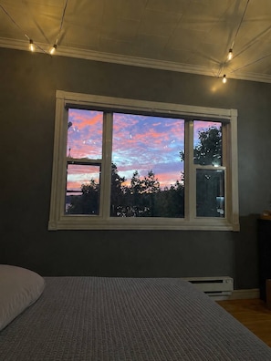 A bedroom with a large window, a bed, and a heater.