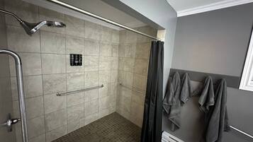 A shower with a handheld showerhead, a grab bar, and a towel rack with towels.
