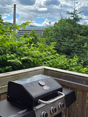 A barbecue grill on a balcony with a view of a cruise ship in the background.