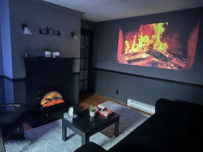 Uma sala de estar com lareira, uma televisão exibindo uma chama e um sofá.