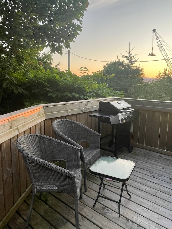 An outdoor deck with wicker chairs, a grill, and a table.