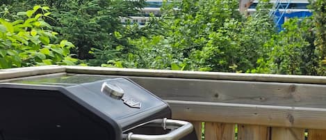 A barbecue grill with a logo, a wooden deck, and a view of a building with a distinctive blue and white logo in the background.
