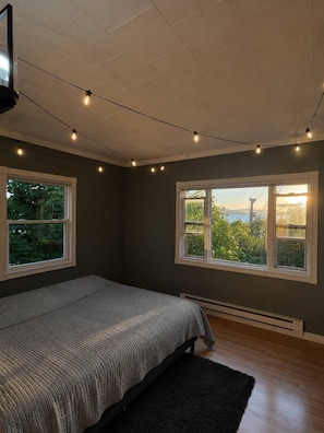 Quarto com cama, duas janelas, ventilador de teto e uma guirlanda de luzes.