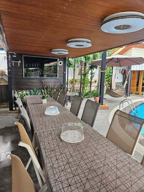 Ett utomhusområde med plats för måltider, komplett med ett långt bord, stolar och en pool.